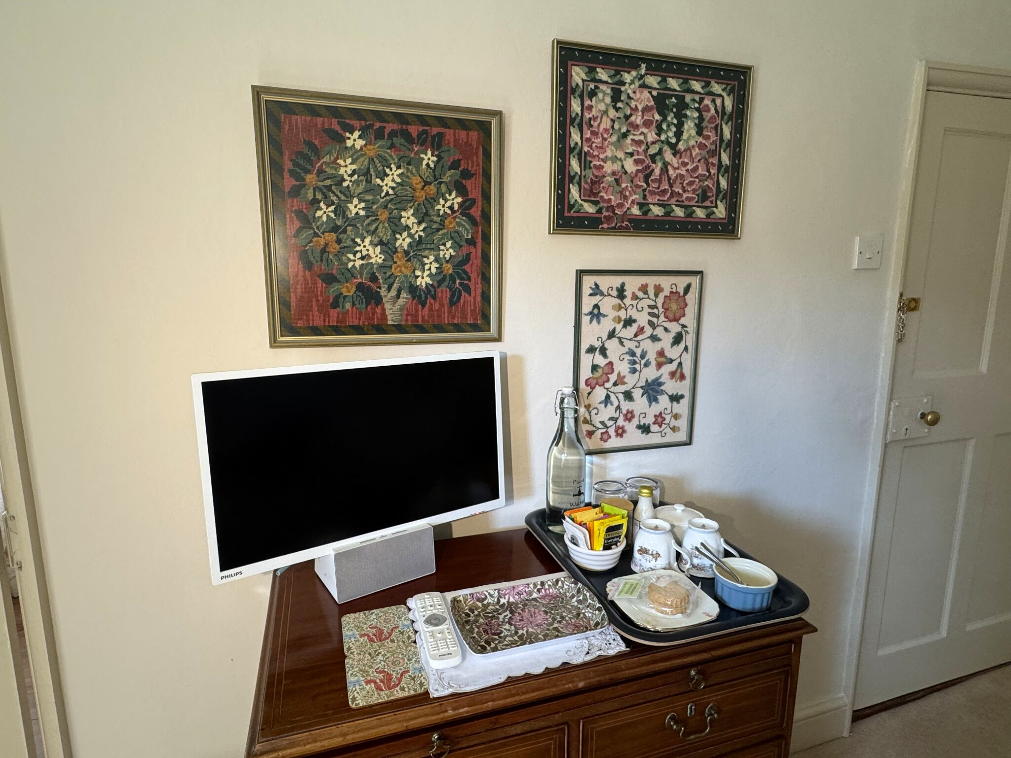 Una habitación con televisión de pantalla plana, un mueble de madera con varios objetos, y tres cuadros con motivos florales en la pared.
