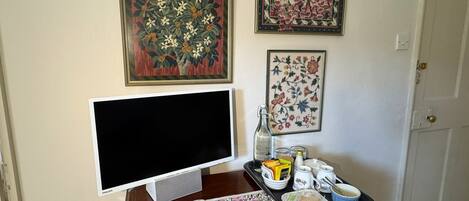 Una habitación con televisión de pantalla plana, un mueble de madera con varios objetos, y tres cuadros con motivos florales en la pared.