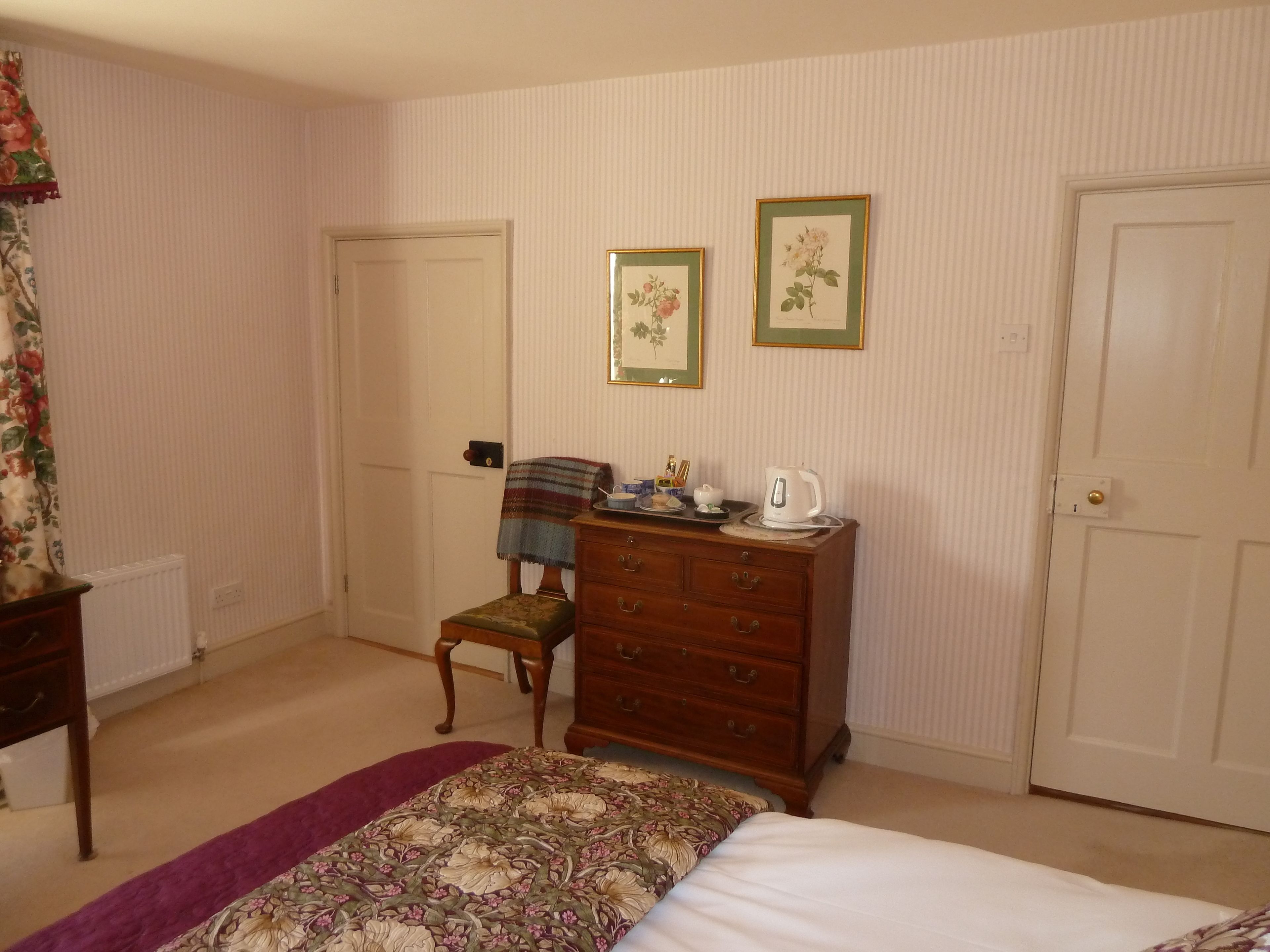 A bedroom with a bed, a dresser, a chair, a radiator, and two framed pictures on the wall.