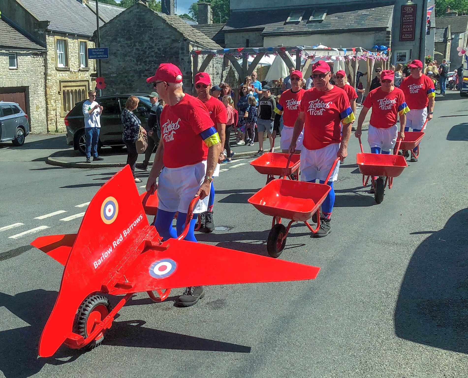 A street parade with participants in red uniforms pushing red wheelbarrows.