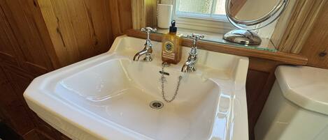 Un baño con un lavamanos blanco, dos grifos, un dispensador de jabón y un inodoro.