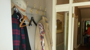 A hallway with a coat rack holding several coats and a scarf, a pair of boots, and a door leading to another room. - The Old Vicarage B&B (Buxton)