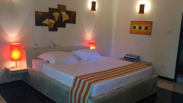 A neatly made bed with white linens and a striped blanket, two bedside lamps, and a wall-mounted artwork of flowers.