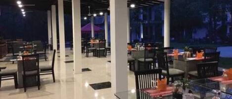 An indoor dining area with tables and chairs, large pillars, and a ceiling with exposed beams.