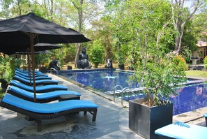 A pool area with lounge chairs and umbrellas, surrounded by greenery.