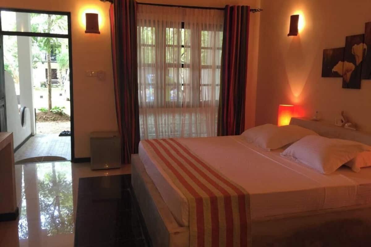 Ein Hotelzimmer mit Bett, Vorhängen, einer Wandlampe und einer zur Außenwelt führenden Tür.