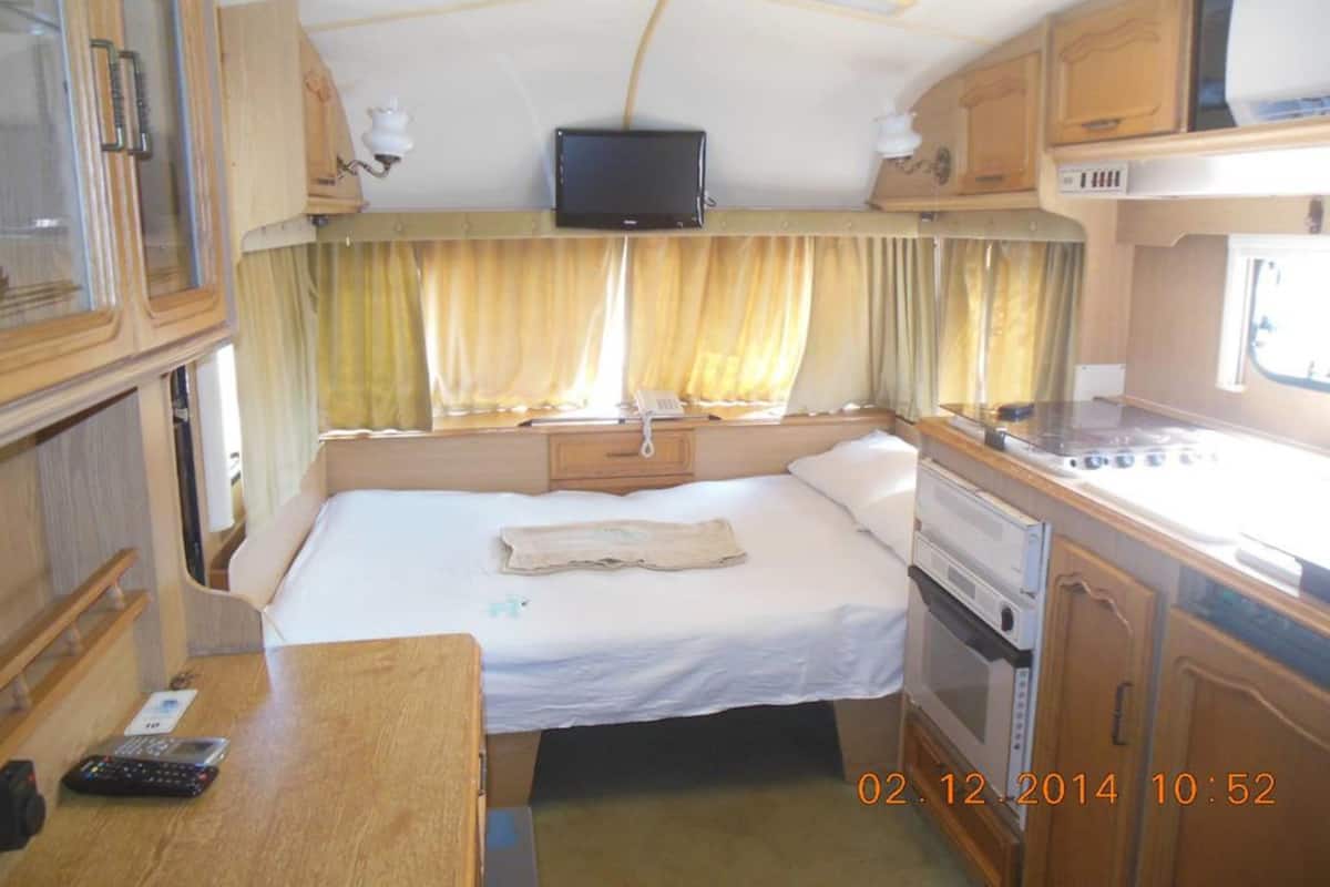 Un intérieur de camping-car compact comprenant un lit, un coin cuisine et un téléviseur fixé au mur.