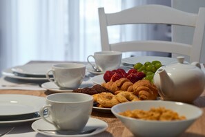 Et morgenbord med tallerkener, kopper og et udvalg af kager og frugt.
