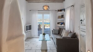 A cozy living room with a glass coffee table, a sofa, and a TV. There is a view of the sea through a large window. - Nalu Villa Mykonos (Mykonos)