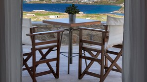 A balcony with a table and chairs, overlooking a coastal town with buildings and the sea. - Nalu Villa Mykonos (Mykonos)