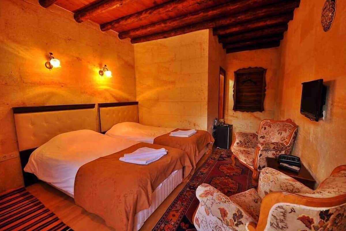 A room with two beds, a chair, a small table, and a wall-mounted TV.