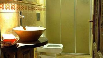 A bathroom with a wooden vanity, a large bowl sink, a toilet, and a shower area.
