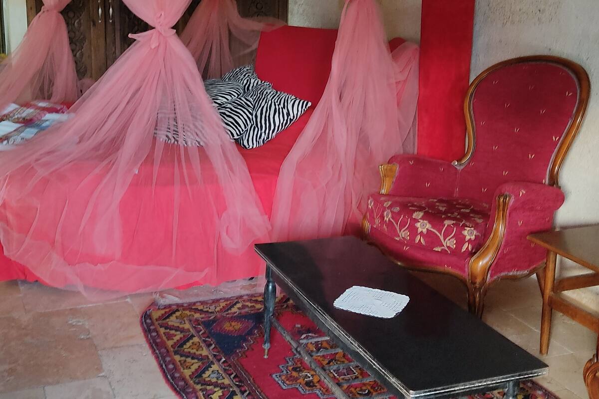 A room with a canopy bed, a red sofa, a red armchair, and a small table.