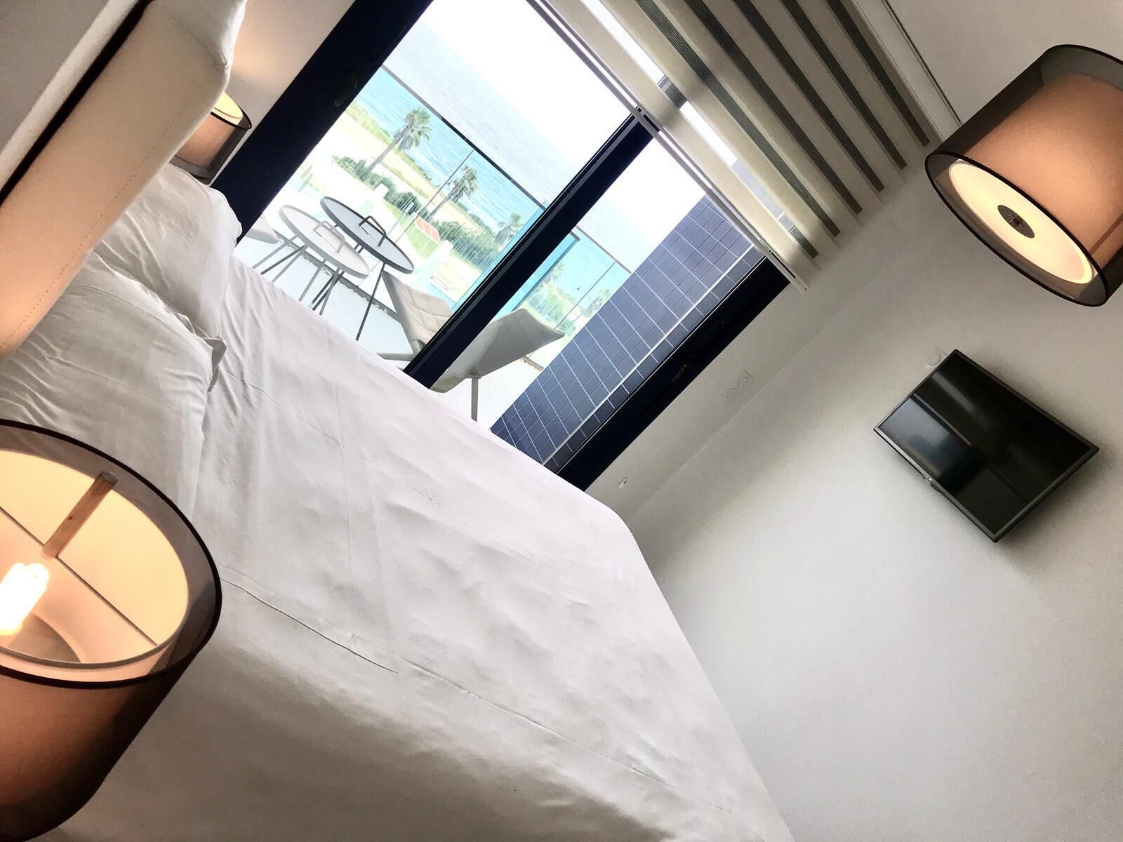 Habitación de hotel con cama, televisión y vista a una piscina y palmeras.