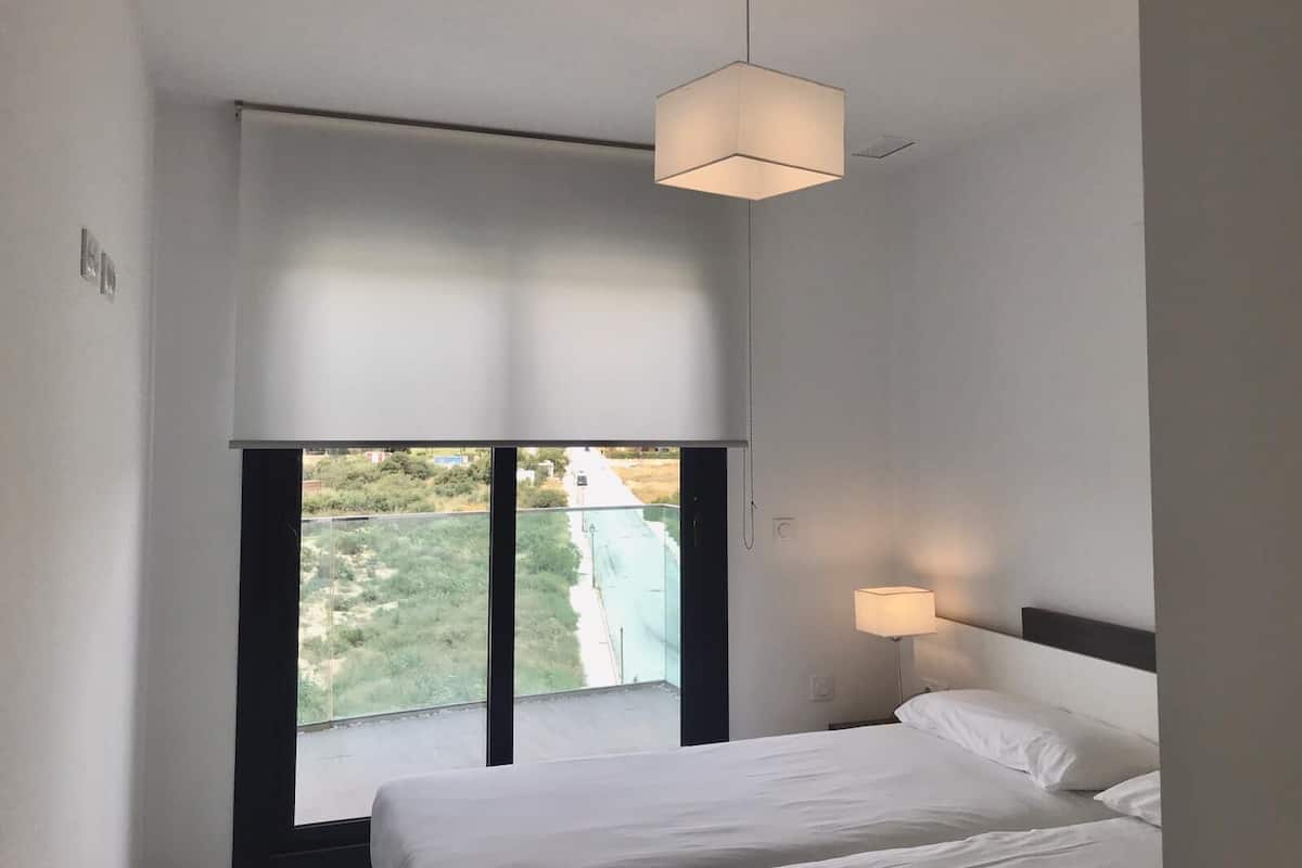 Een hotelkamer met een groot raam, een bed, een nachtkastje en een hanglamp.
