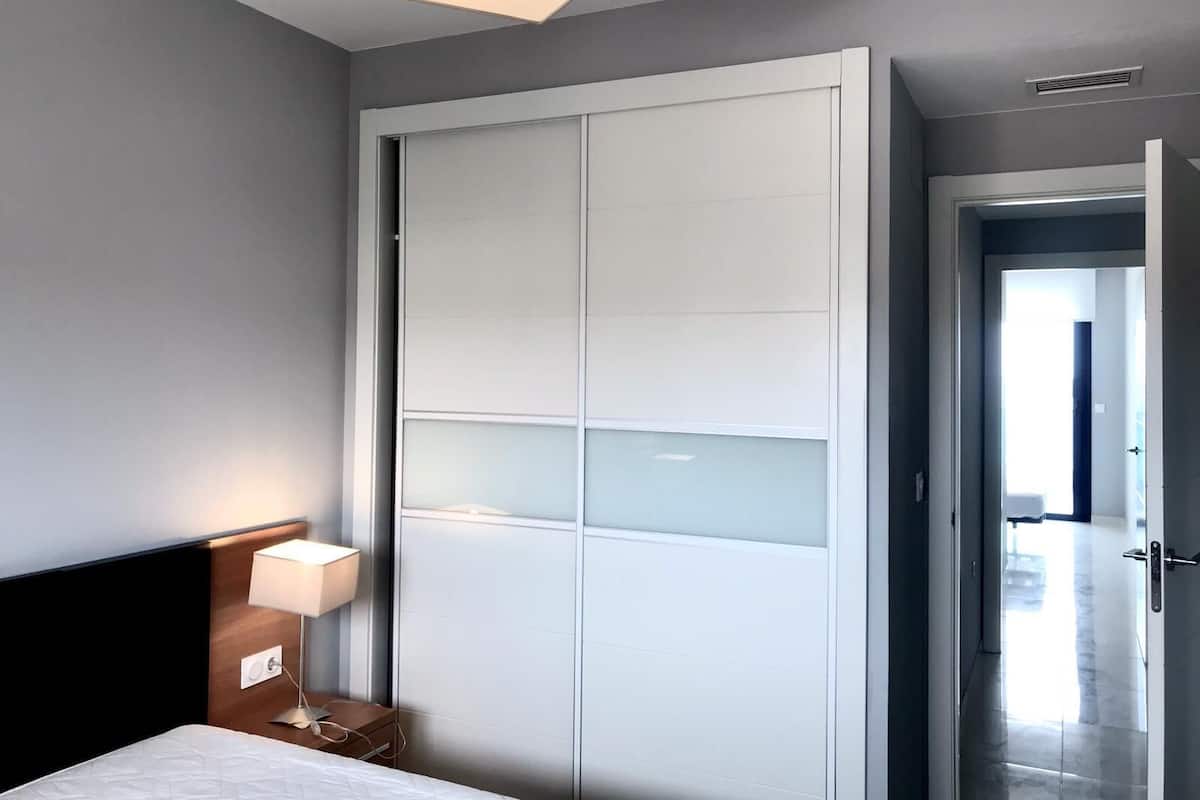 Een moderne slaapkamer met een bed, een bedlampje en een grote garderobe met gebarsten glazen deuren.