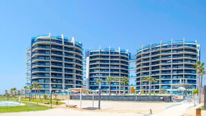 A modern hotel with multiple curved balconies, a pool area, and palm trees. - Sea Senses Apartments - Marholidays (Torrevieja)