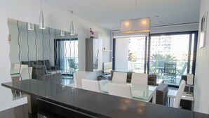 A modern kitchen with a large island, glass dining table, and contemporary lighting fixtures. - Sea Senses Apartments - Marholidays (Torrevieja)