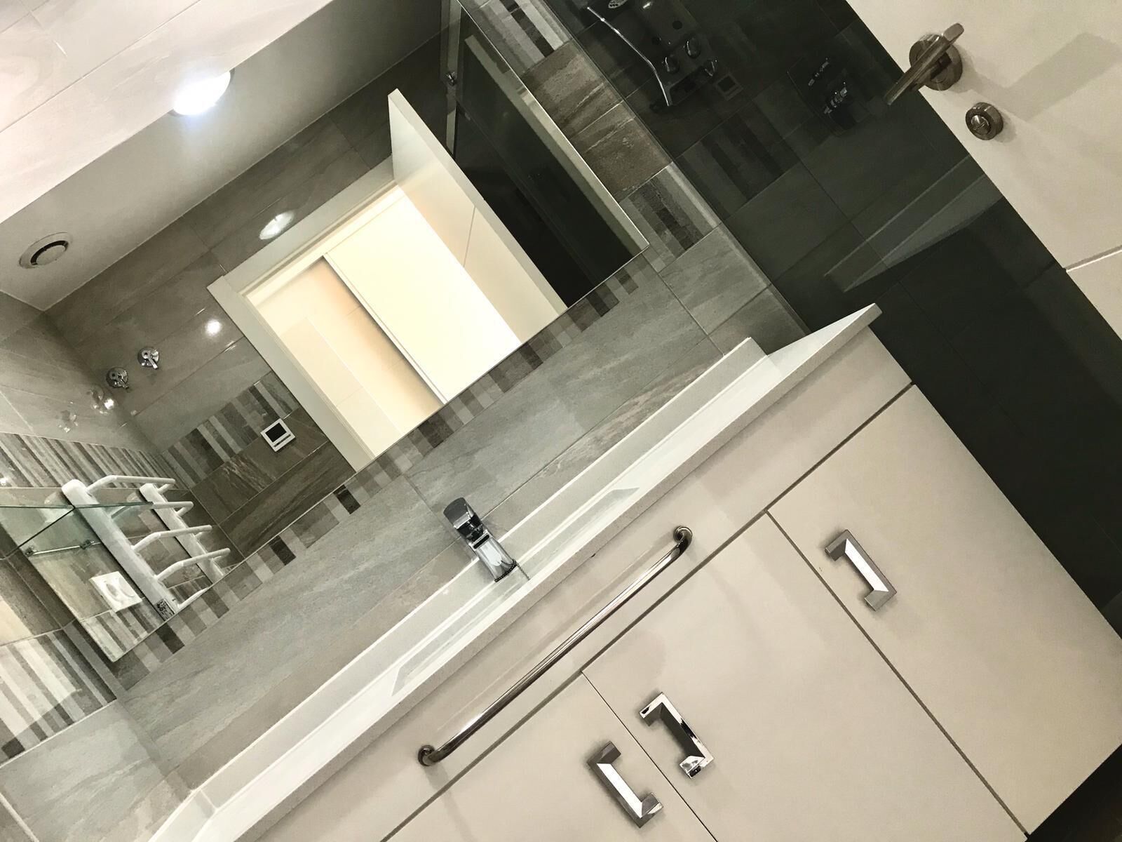 Un baño moderno con cabina de ducha de vidrio, lavamanos blanco y espejo.