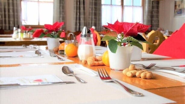 A dining table set with white placemats, silverware, a glass pitcher, a glass of orange juice, a bottle of milk, and a potted plant with red leaves.