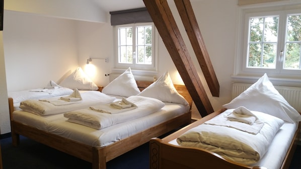A room with two wooden beds, each with white linens and pillows, and a sloped ceiling with exposed beams.