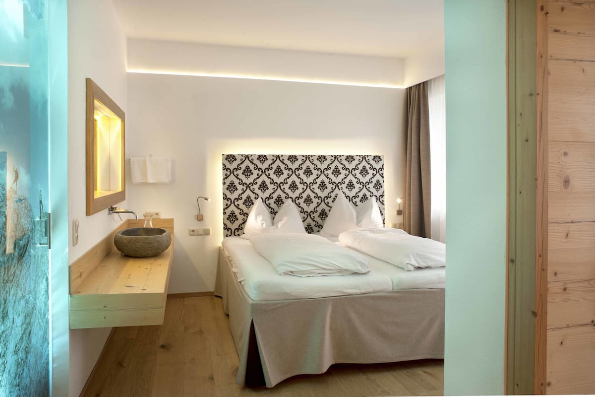 A hotel room with a wooden bedside table, a stone basin, a patterned headboard, and a bed with white linens.