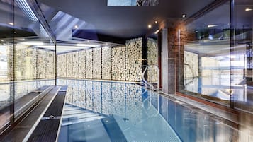 Una piscina interior moderna con paredes de vidrio y un revestimiento de pared decorativo.