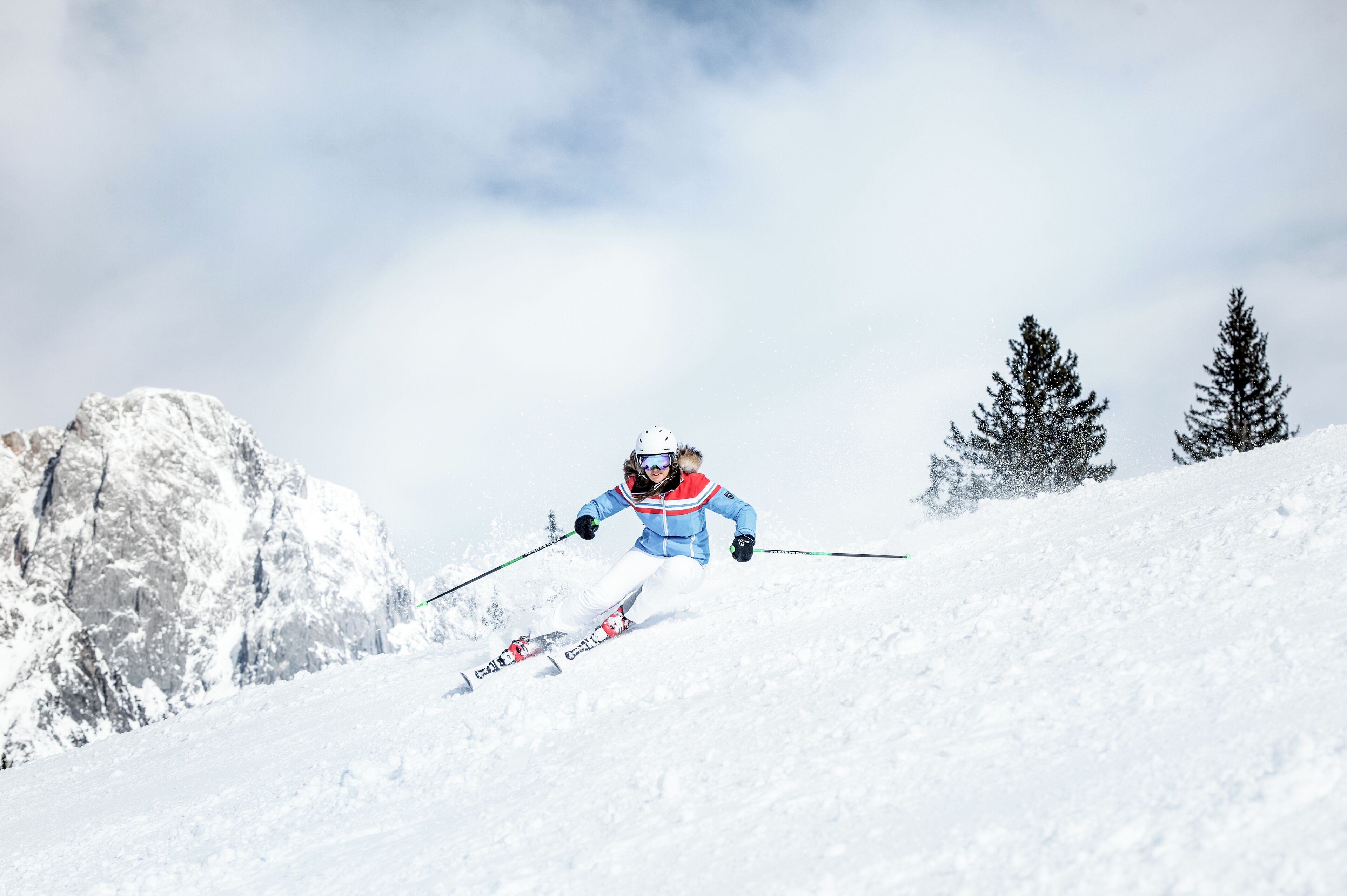 A skier on a snowy slope with rocky terrain and sparse trees.