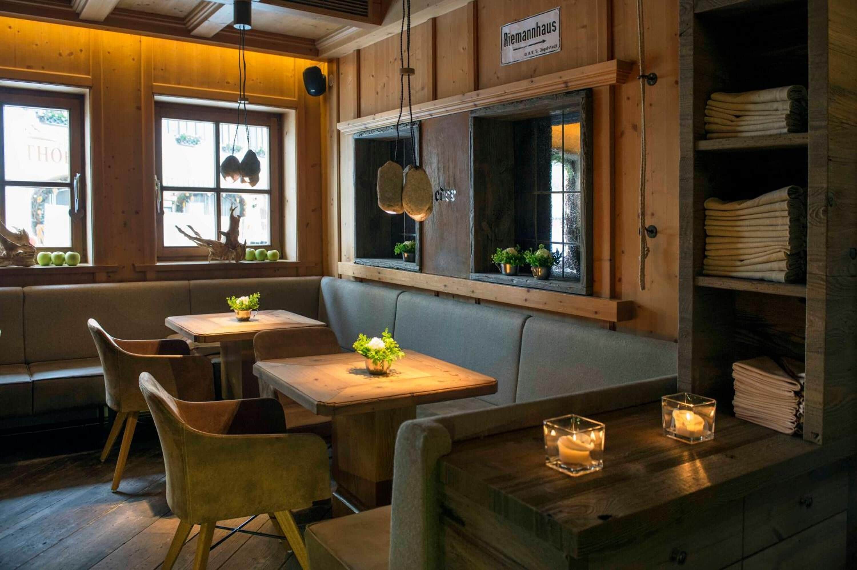 En mysig restaurang med träpanel på väggarna, en sittgrupp med bänkar och bord med levande ljus.