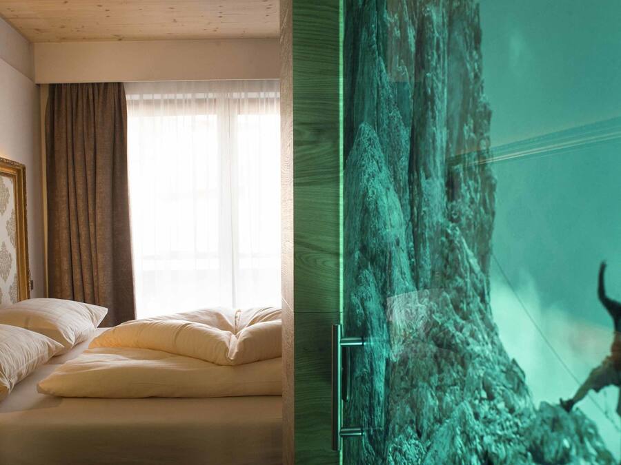 A room with a bed, a window with curtains, and a wall with a patterned wallpaper.