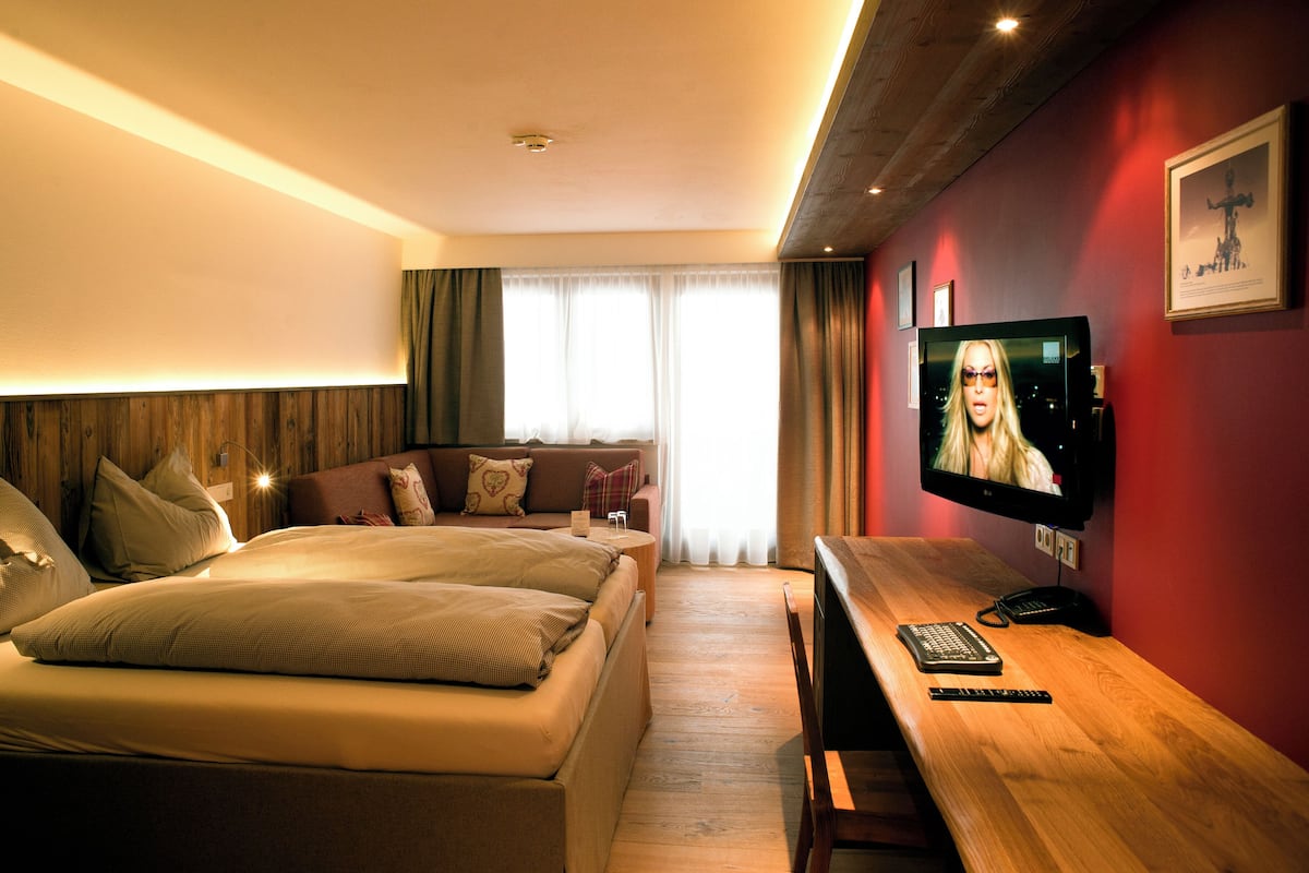 A hotel room with two beds, a TV, a wooden desk, and a window with curtains.