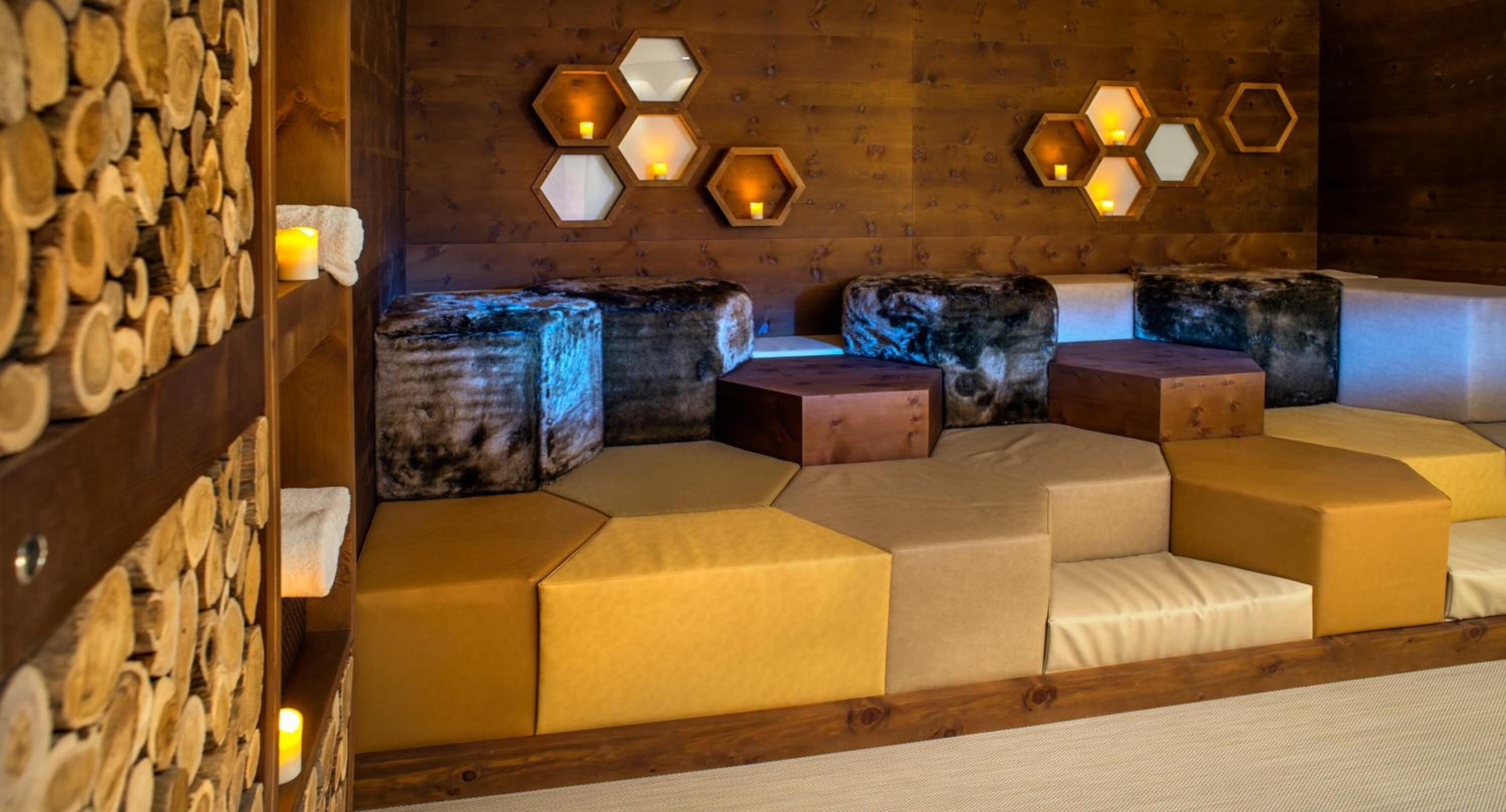 A cozy room with hexagonal wall sconces, a wooden wall with logs, and a seating area with cushioned benches.