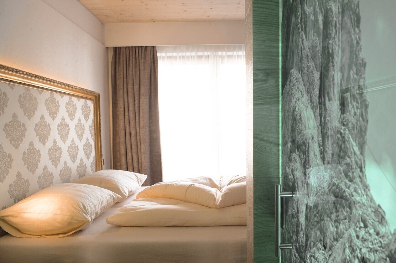 Un dormitorio con cama, cabecera con diseño estampado, ventana con cortinas y pared con textura.