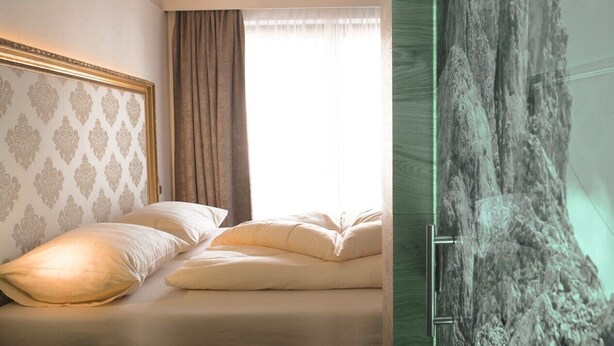 A bedroom with a bed, a headboard with a patterned design, a window with curtains, and a wall with a textured surface. - Lifestyle Hotel eder (Maria Alm am Steinernen Meer)
