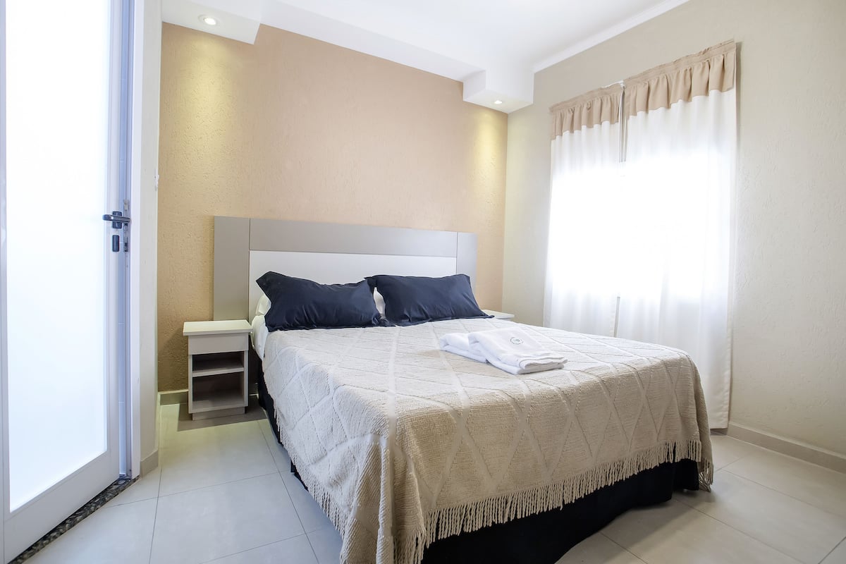 A bedroom with a bed, nightstand, and a window with curtains.