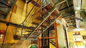 Un interior de varios niveles con paredes de ladrillo visto, escaleras de metal y un ventanal con tonalidad verdosa.