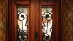 Puerta doble de madera con tallas elaboradas y un panel de vidrio con diseño metálico.