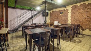 Un restaurante con paredes de ladrillo, mesas y sillas de madera. Se ve una escalera con un televisor en la pared.