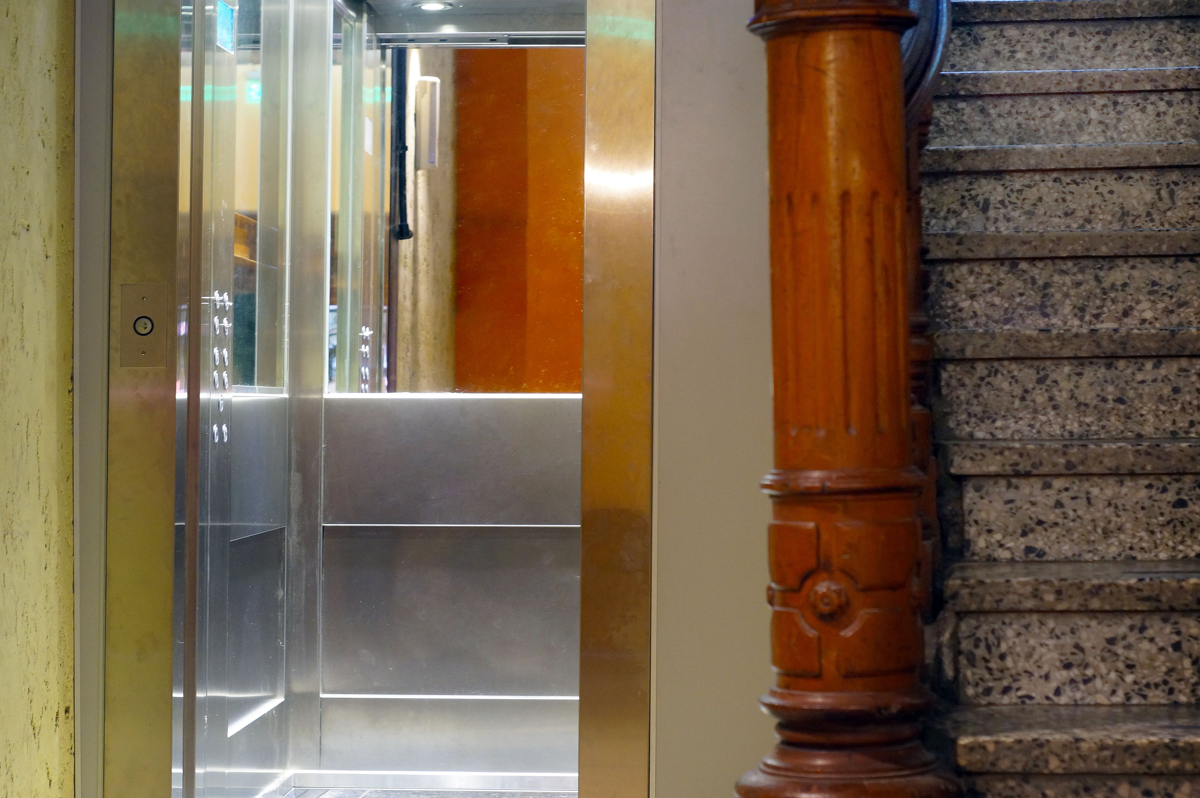 An elevator interior with metallic walls and a wooden column.