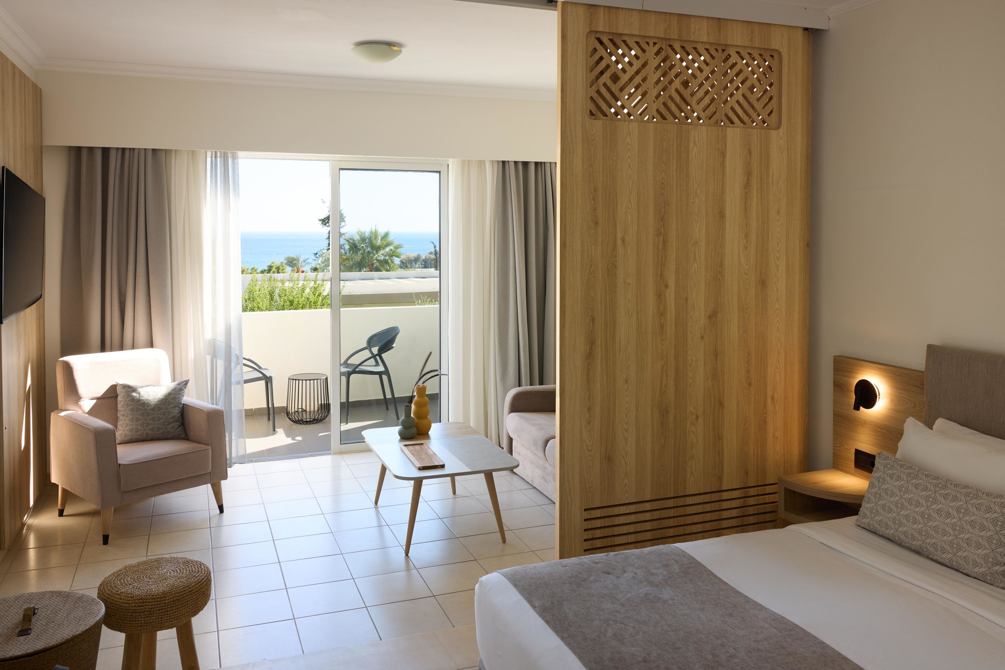 Una habitación de hotel moderna con una cama, un sofá, una mesita y vistas al océano a través de amplios ventanales.