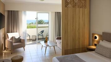 Una habitación de hotel moderna con una cama, un sofá, una mesita y vistas al océano a través de amplios ventanales.