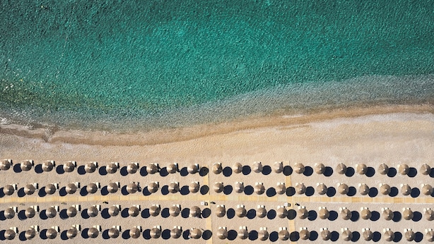 Une plage bordée d’une rangée de chaises longues alignées parallèlement au rivage.