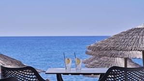 Une table avec deux verres contenant une boisson, une paille et une tranche de citron, le tout placé sur fond d’océan et de ciel dégagé.