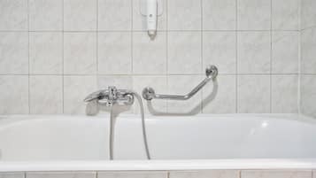 Una bañera blanca con ducha de mano y barra de apoyo, frente a una pared azulejada.