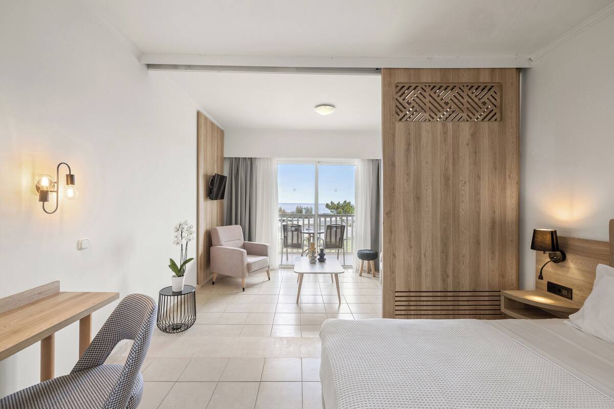 Une chambre d’hôtel moderne équipée d’un lit, d’un bureau, d’une chaise, d’une petite table et d’un balcon avec vue.