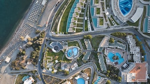 Vue aérienne d  ’un complexe hôtelier doté de plusieurs piscines, d’une place centrale circulaire et d’une zone de plage avec des parasols.