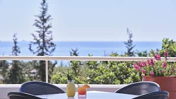A balcony with a table, two chairs, a glass of a yellow drink, a glass of a red drink, and a potted plant with pink flowers.