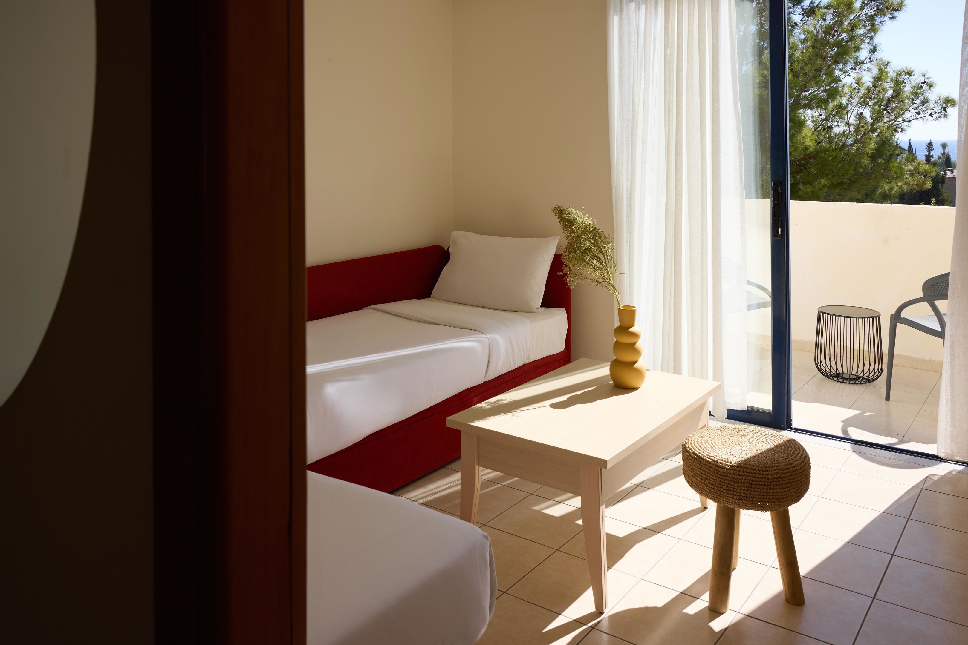 Una habitación moderna con un sofá rojo y blanco, una pequeña mesa de madera y un taburete de mimbre.