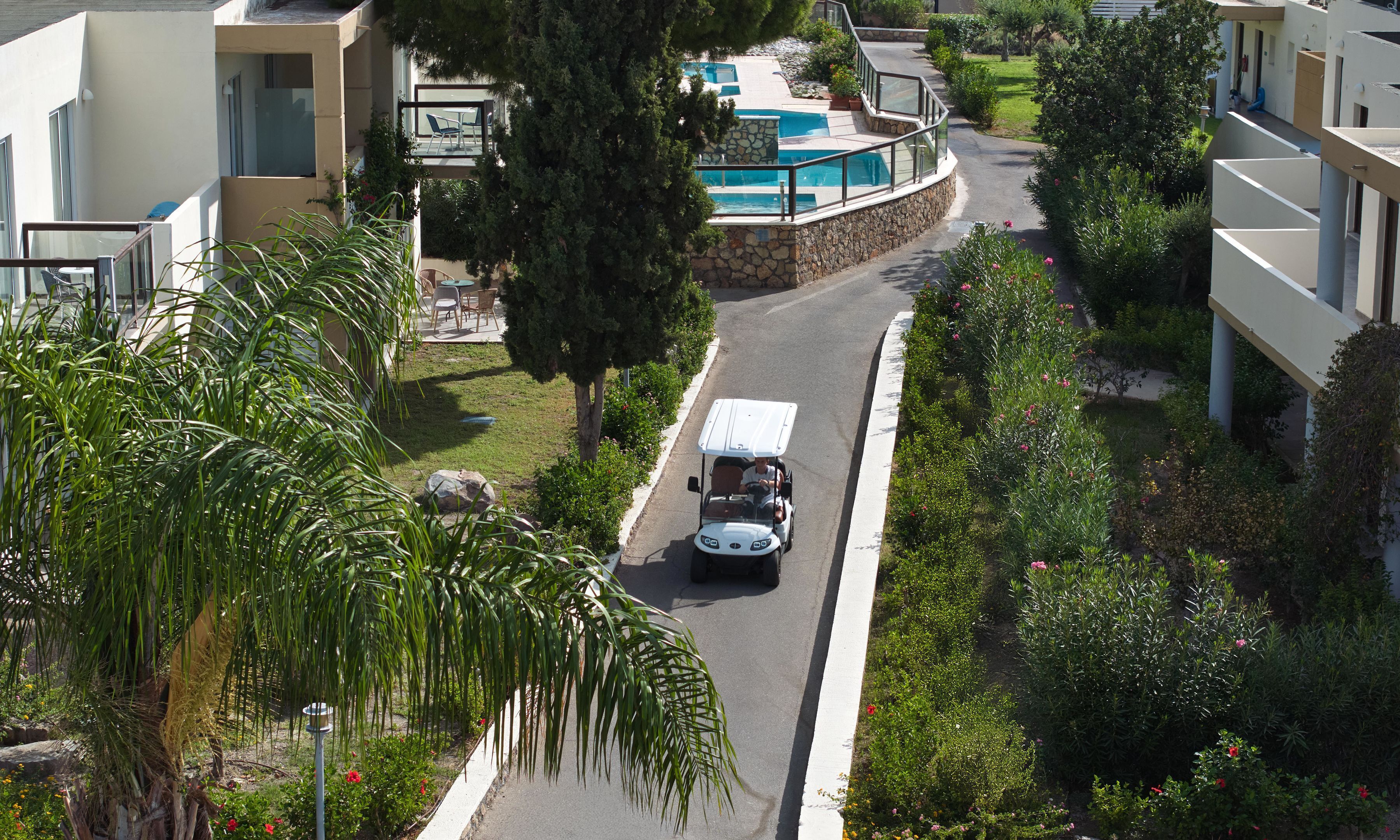 A residential street with a golf cart, a swimming pool, and lush greenery.