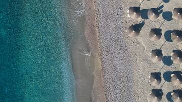 Vista aérea de una playa con agua turquesa cristalina y una orilla arenosa. Sombrillas están alineadas a lo largo de la playa.